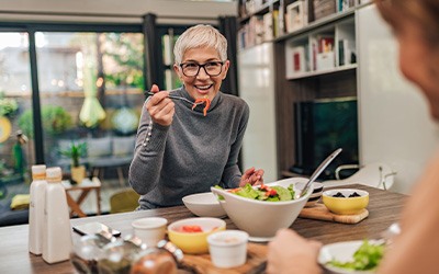 Woman smiling while eating lunch with friend in kitchen