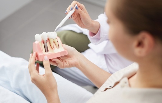 Dentist and patient looking at dental implant model and discussing the cost of tooth replacement with dental implants