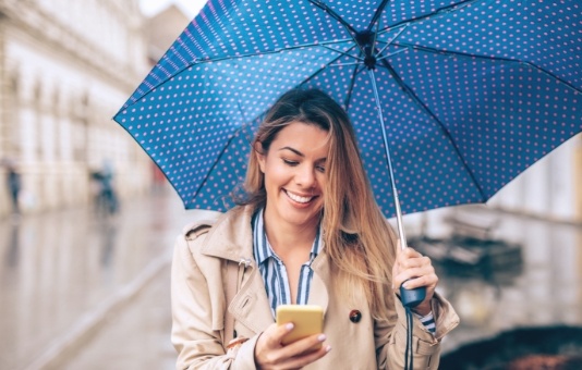 Smiling woman under an umbrella looking at her phone