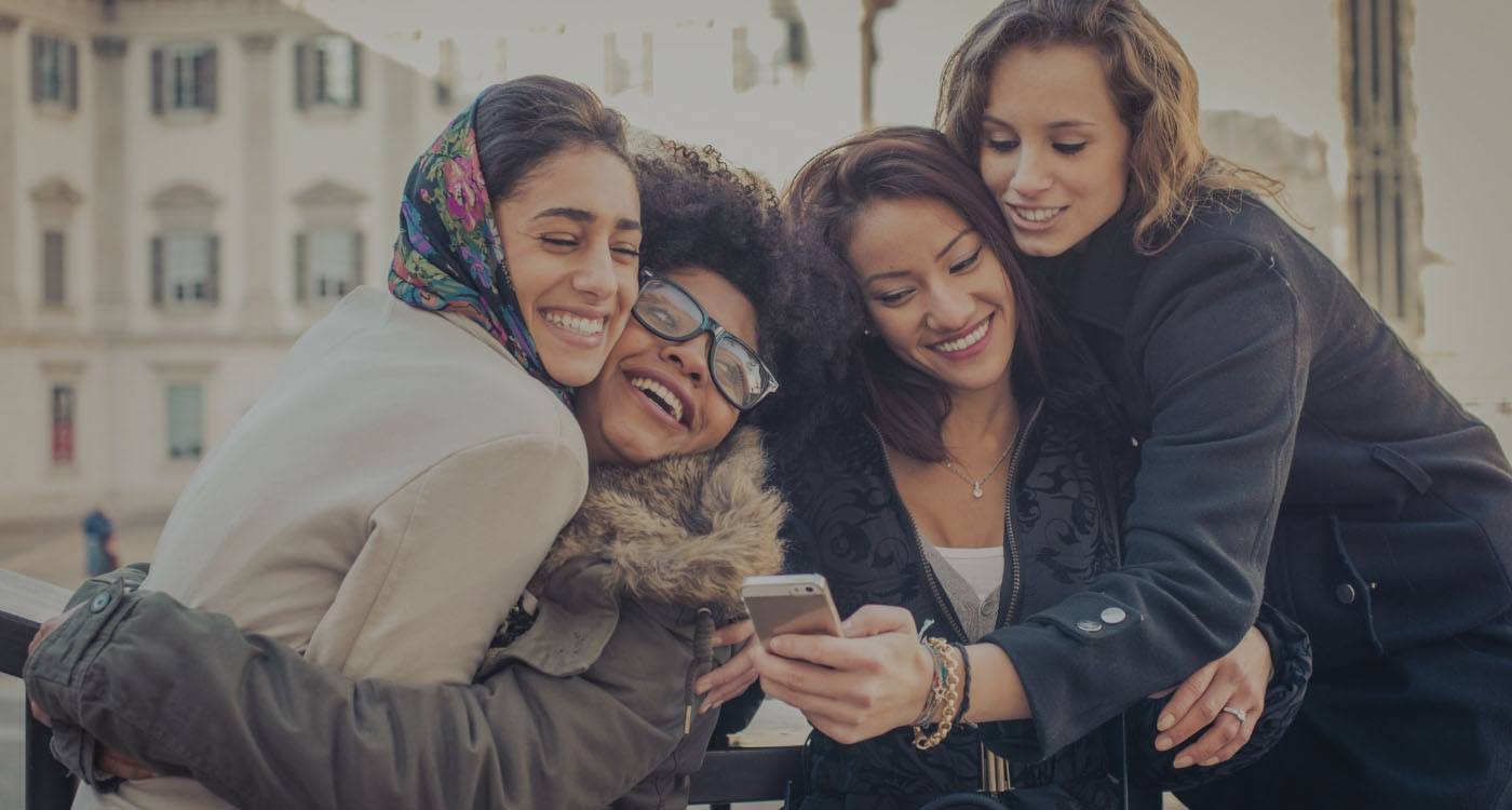 Four smiling women taking selfie together outdoors