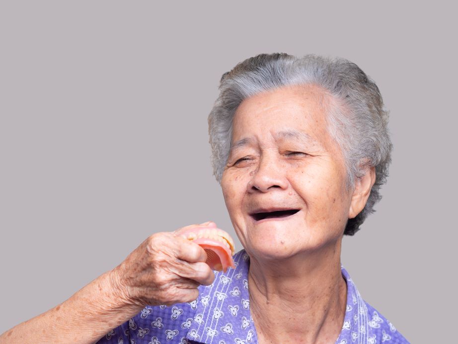 A senior with no teeth holding a denture